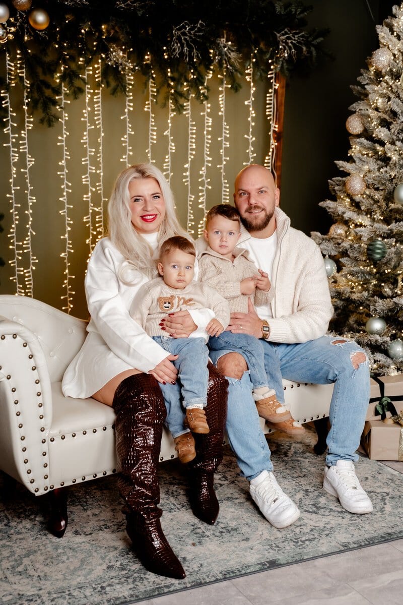 Familie mit zwei kleinen Kindern auf einem weißen Sofa vor einer Lichterkette im Weihnachtsstudio