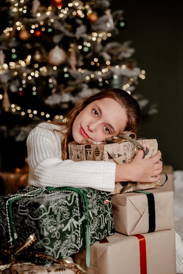 Mädchen im weißen Strickpullover, den Kopf auf einen Stapel Geschenke gelegt